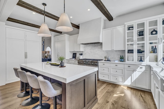 kitchen with white cabinetry, light wood-type flooring, custom range hood, beamed ceiling, and a center island