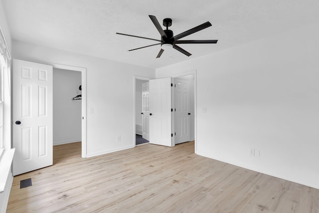 unfurnished bedroom with ceiling fan, a textured ceiling, light wood-type flooring, a closet, and a walk in closet