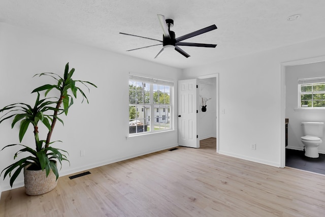 bedroom with connected bathroom, ceiling fan, multiple windows, and light hardwood / wood-style flooring