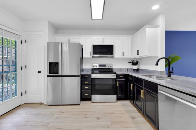 kitchen with light stone counters, appliances with stainless steel finishes, white cabinetry, light hardwood / wood-style flooring, and sink