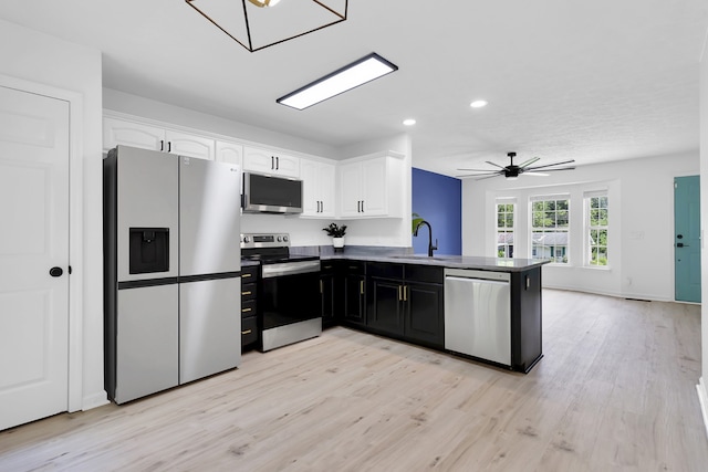 kitchen with kitchen peninsula, white cabinets, appliances with stainless steel finishes, light wood-type flooring, and sink