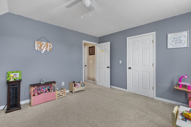 recreation room featuring a textured ceiling, light colored carpet, and ceiling fan