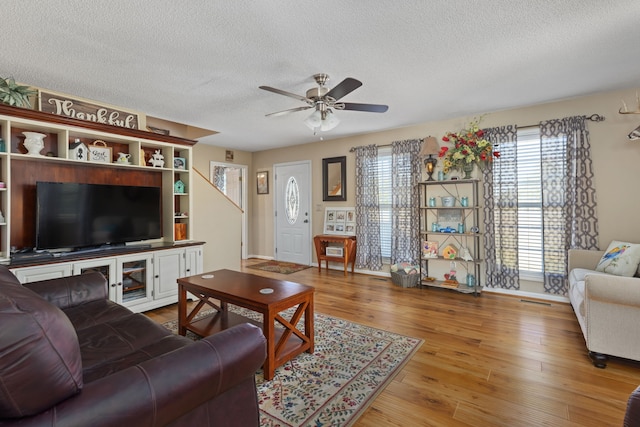 living room with ceiling fan, a textured ceiling, and light wood-type flooring