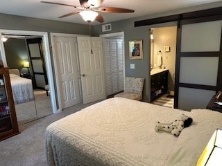 carpeted bedroom with ceiling fan, ensuite bath, multiple closets, and a barn door