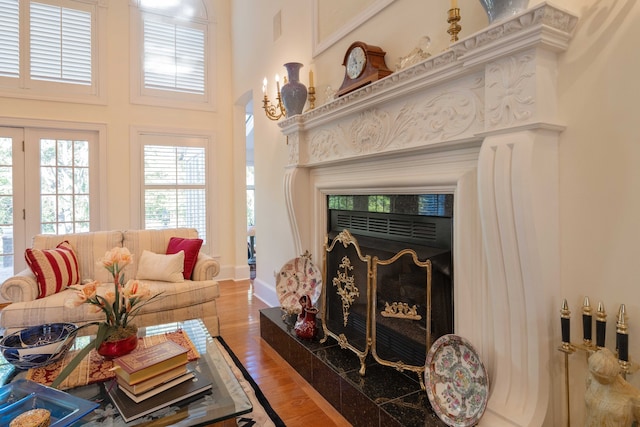 living room with a premium fireplace, wood-type flooring, and a towering ceiling