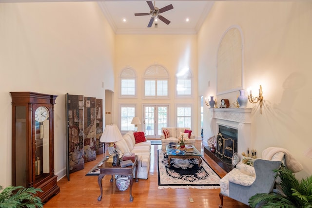 living room featuring light hardwood / wood-style floors, a towering ceiling, ornamental molding, and ceiling fan