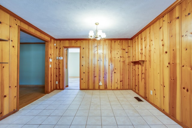 tiled spare room with crown molding, wood walls, and a chandelier