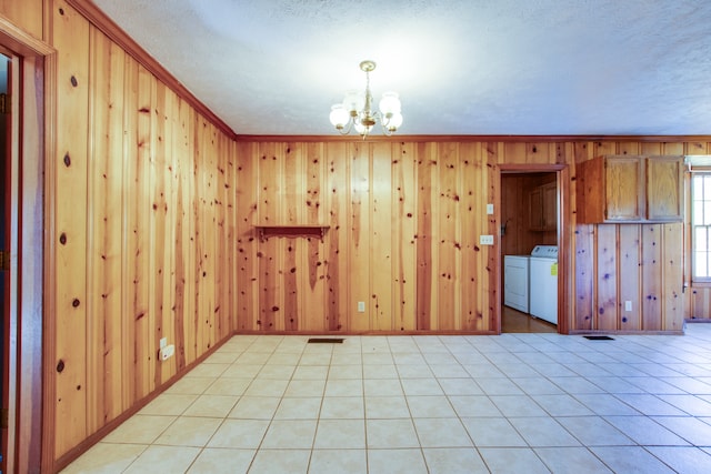 unfurnished room with washer and dryer, wood walls, light tile patterned flooring, ornamental molding, and an inviting chandelier