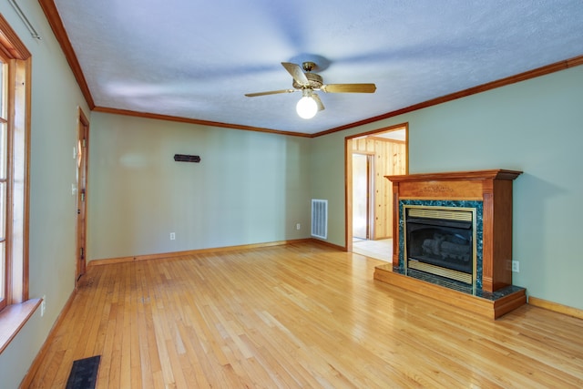 unfurnished living room featuring a high end fireplace, ornamental molding, light hardwood / wood-style floors, and ceiling fan