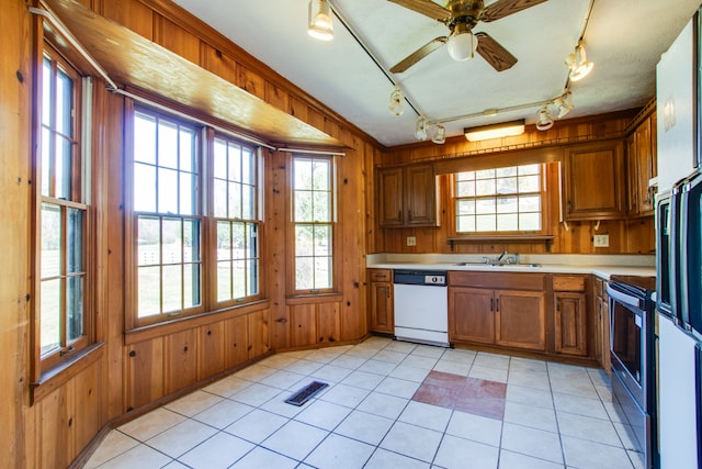 kitchen with dishwasher, wooden walls, track lighting, and plenty of natural light