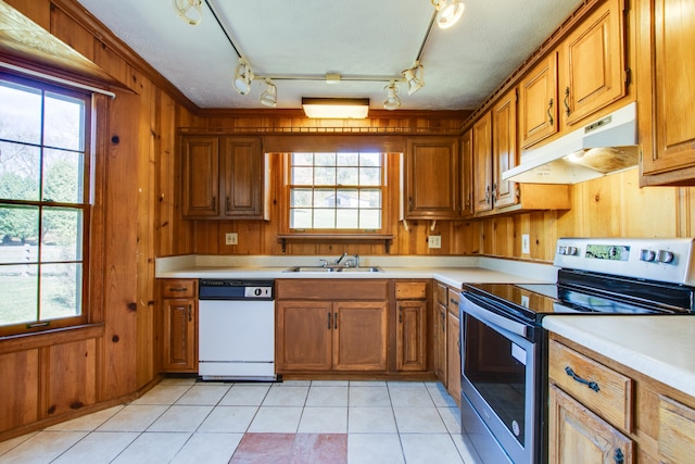 kitchen featuring light tile patterned floors, wood walls, dishwasher, stainless steel range with electric stovetop, and sink