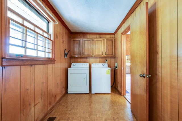 laundry area featuring washer and dryer, wood walls, light parquet floors, ornamental molding, and cabinets