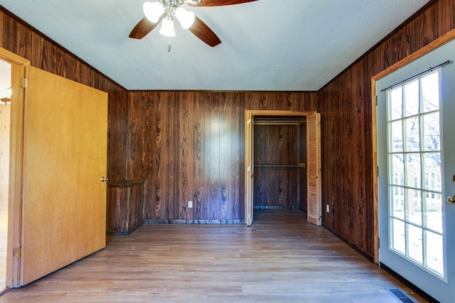 empty room with wood walls, a textured ceiling, light wood-type flooring, and ceiling fan