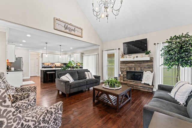 living room featuring a stone fireplace, dark wood-type flooring, ornamental molding, a notable chandelier, and high vaulted ceiling