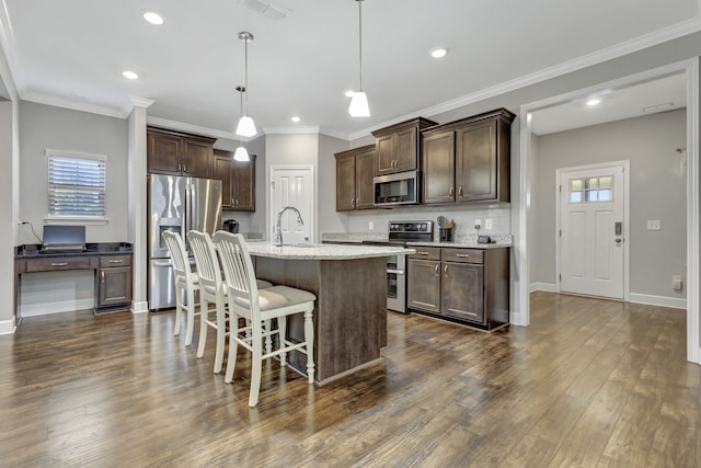 kitchen featuring a kitchen island with sink, dark wood-type flooring, hanging light fixtures, stainless steel appliances, and a kitchen bar