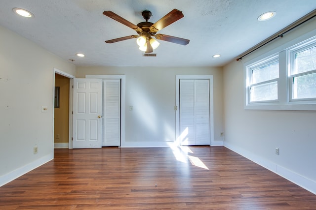 unfurnished bedroom with multiple closets, ceiling fan, a textured ceiling, and dark hardwood / wood-style flooring