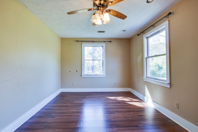 unfurnished room with a wealth of natural light, dark wood-type flooring, a textured ceiling, and ceiling fan