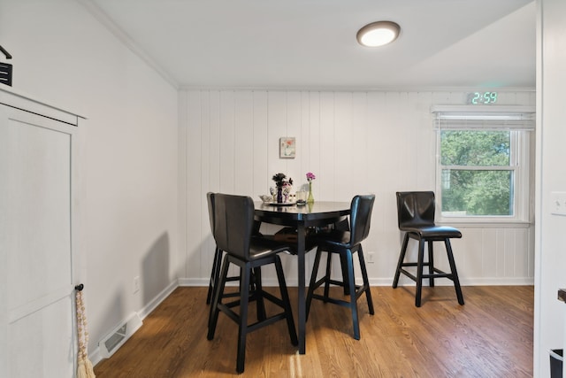 dining area with ornamental molding, wood walls, and hardwood / wood-style floors