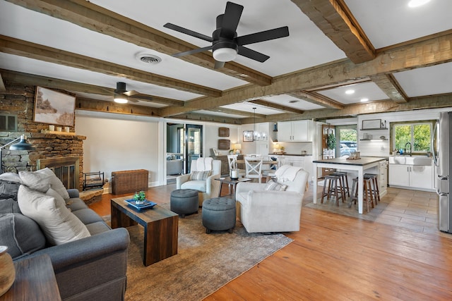 living room featuring sink, light wood-type flooring, a fireplace, ceiling fan, and beam ceiling