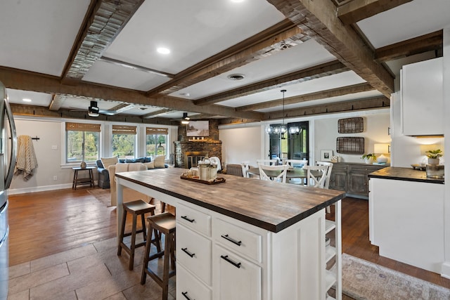 kitchen with wooden counters, light hardwood / wood-style flooring, a large fireplace, pendant lighting, and white cabinetry