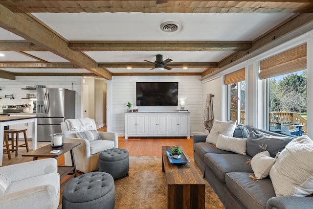 living room with beam ceiling, wooden walls, light wood-type flooring, and ceiling fan