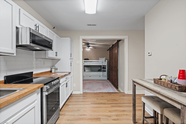 kitchen with decorative backsplash, light hardwood / wood-style flooring, stainless steel appliances, a barn door, and white cabinetry