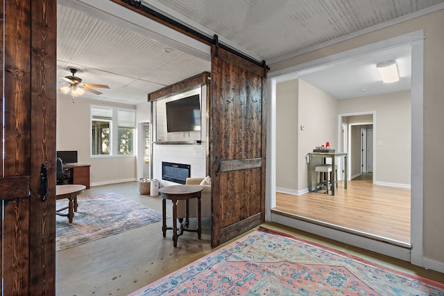 living room with ceiling fan, a large fireplace, a barn door, and concrete flooring