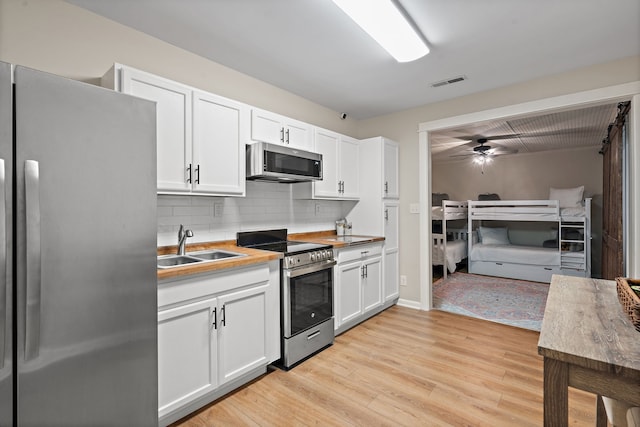 kitchen featuring appliances with stainless steel finishes, backsplash, white cabinetry, light hardwood / wood-style floors, and ceiling fan