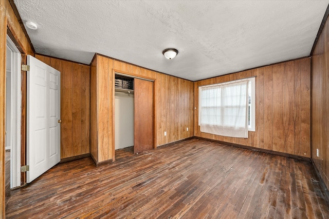 unfurnished bedroom featuring a closet, wood walls, a textured ceiling, and dark hardwood / wood-style floors