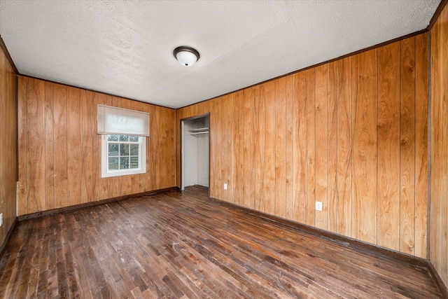 unfurnished bedroom with dark wood-type flooring, a closet, a textured ceiling, and wood walls