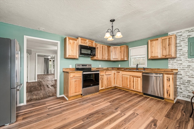 kitchen with appliances with stainless steel finishes, sink, butcher block counters, hanging light fixtures, and light hardwood / wood-style floors