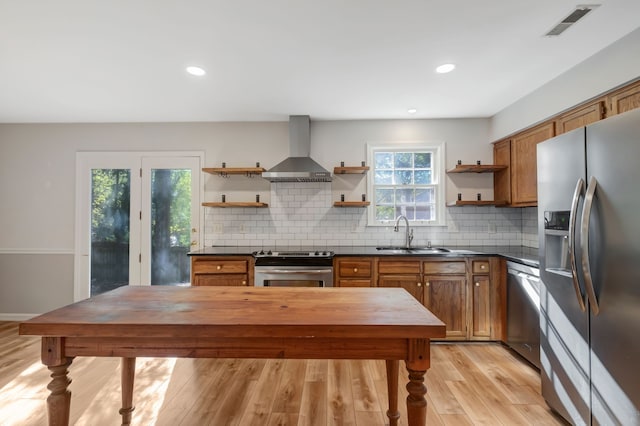 kitchen featuring wall chimney range hood, sink, light wood-type flooring, appliances with stainless steel finishes, and tasteful backsplash