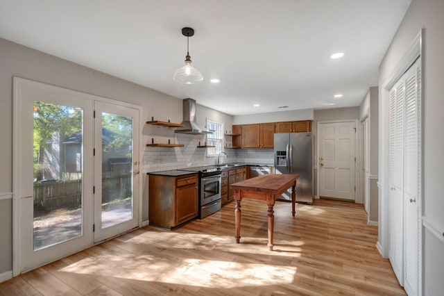 kitchen with wall chimney range hood, sink, pendant lighting, light wood-type flooring, and appliances with stainless steel finishes