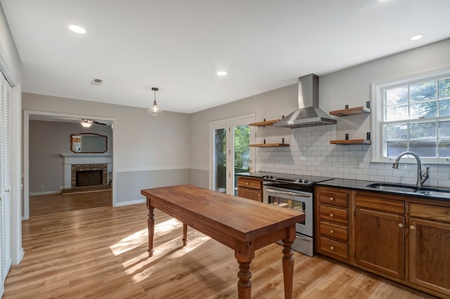 kitchen with sink, plenty of natural light, light hardwood / wood-style floors, wall chimney exhaust hood, and stainless steel range with gas cooktop