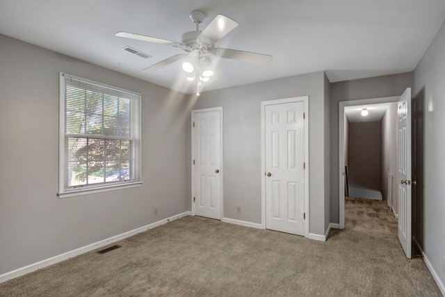 unfurnished bedroom featuring ceiling fan, two closets, and light colored carpet