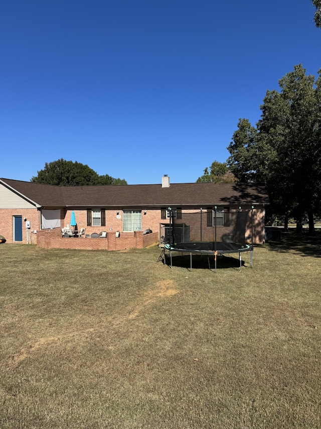 rear view of property with a yard and a trampoline