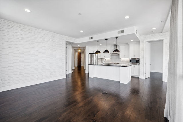 kitchen featuring wall chimney exhaust hood, dark wood-type flooring, a center island, decorative light fixtures, and white cabinetry