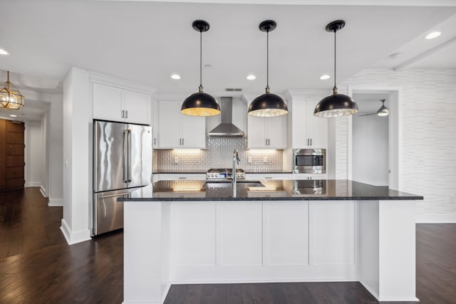 kitchen with hanging light fixtures, appliances with stainless steel finishes, wall chimney range hood, and white cabinetry