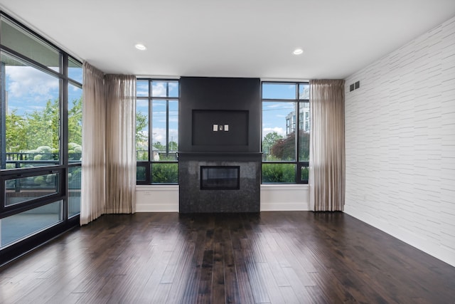 unfurnished living room featuring dark hardwood / wood-style flooring, brick wall, and a wealth of natural light