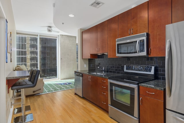 kitchen featuring stainless steel appliances, sink, light wood-type flooring, and backsplash