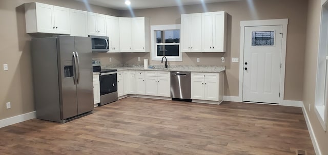 kitchen featuring light stone countertops, stainless steel appliances, sink, light hardwood / wood-style flooring, and white cabinetry