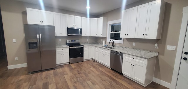 kitchen with light stone counters, stainless steel appliances, dark wood-type flooring, sink, and white cabinets