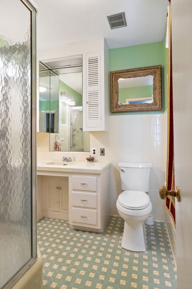 full bathroom featuring vanity, toilet, combined bath / shower with glass door, and tile walls