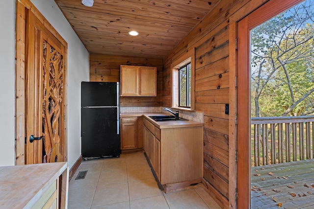 kitchen with light tile patterned floors, wood walls, sink, and black refrigerator