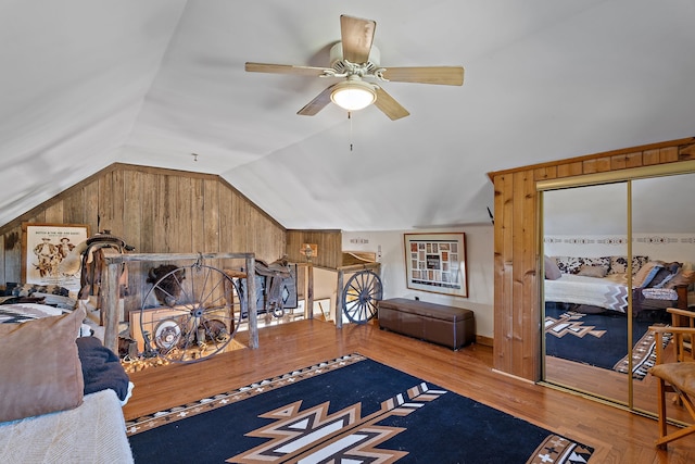 bedroom with wooden walls, vaulted ceiling, light hardwood / wood-style floors, and ceiling fan