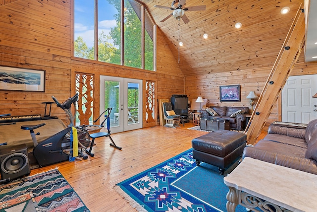 living room with high vaulted ceiling, wood walls, french doors, ceiling fan, and hardwood / wood-style flooring