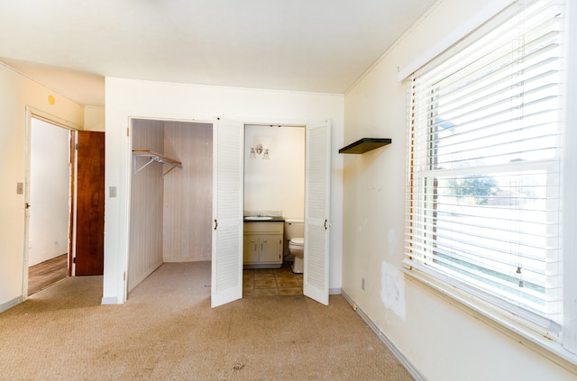 unfurnished bedroom featuring light colored carpet, a closet, and ensuite bath