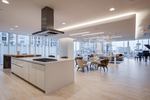 kitchen with island exhaust hood, a kitchen island, a wall of windows, white cabinetry, and stainless steel gas stovetop