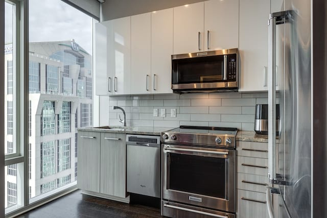 kitchen with backsplash, stainless steel appliances, sink, stone counters, and white cabinetry