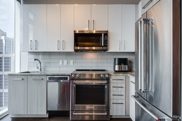 kitchen featuring white cabinets, sink, light stone countertops, appliances with stainless steel finishes, and tasteful backsplash